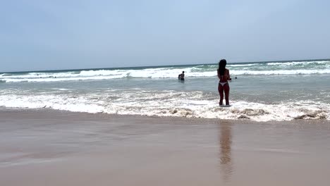 in caparica, a fit woman in a bikini elegantly wets her feet in the seawater, showcasing her side view with confidence and grace with ocean in background