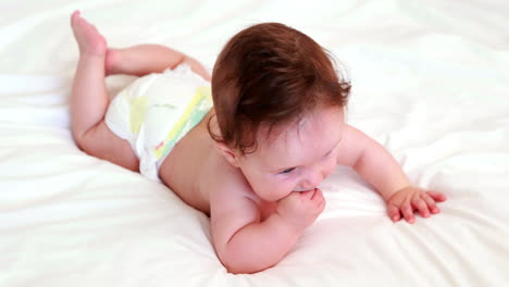 baby in diaper lying on bed