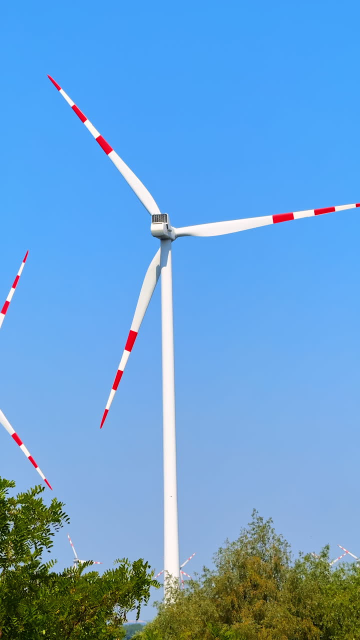 Wind turbine blades rotate slowly in the blue sky. Wind mills over the trees. Vertical video