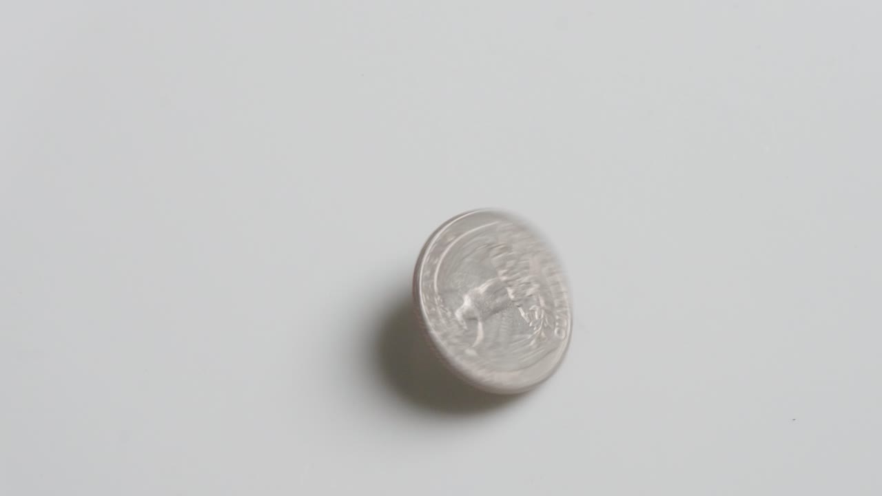 Una singola moneta d'argento che gira su una superficie bianca prima di fermarsi. Moneta da un quarto di dollaro degli Stati Uniti (USD)