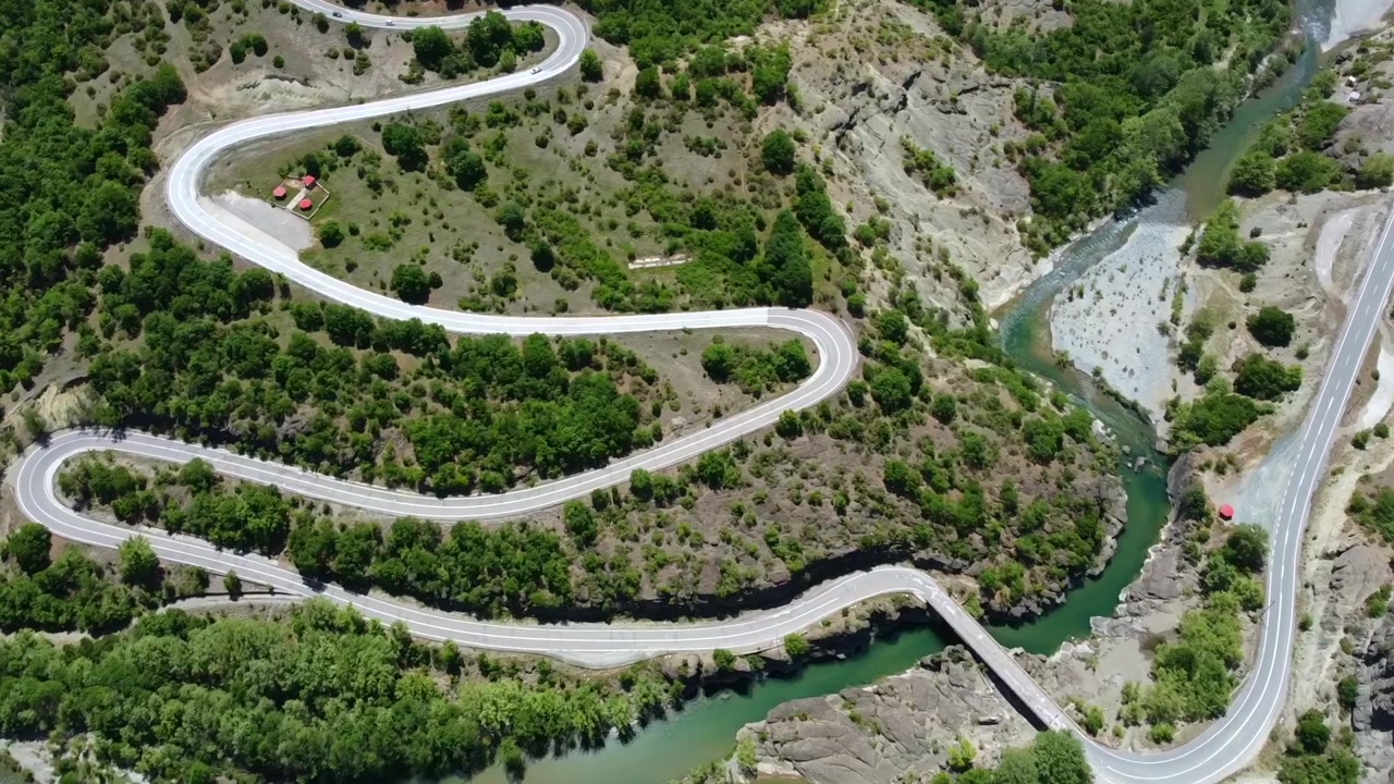 Cinematic drone shot of an epic winding road passing through a rugged canyon. High-angle view of the zig-zag route and the turquoise river below. Ideal for adventure travel and road trip storytelling.
