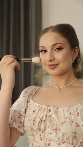 young woman in floral dress gracefully applies makeup with a brush, showcasing beauty and elegance
