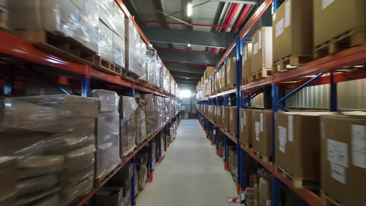 Camera moving through warehouse aisles filled with cardboard boxes on metal shelves, showcasing storage and logistics