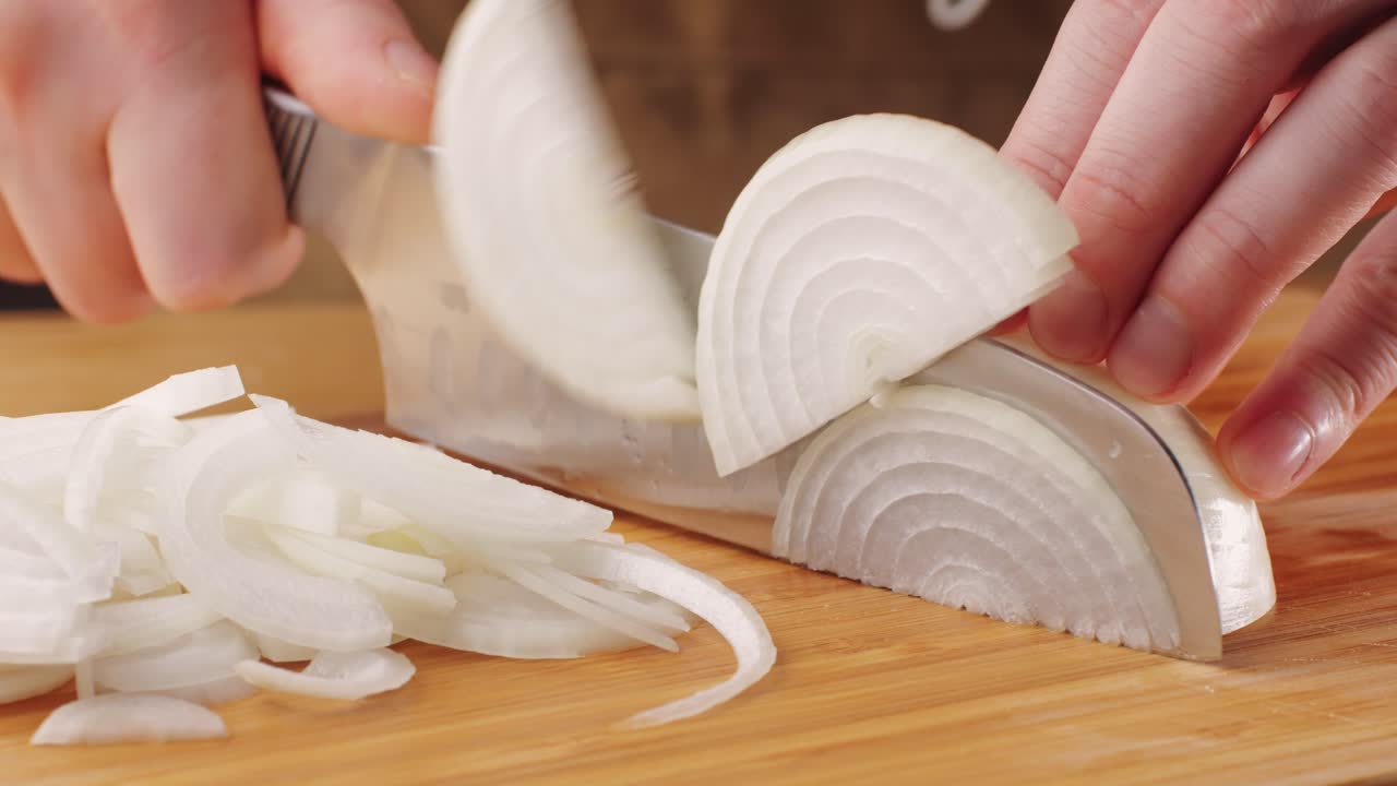 Chef chopping a red onion with a knife on the cutting board, macro close up of cutting red onion on professional kitchen.