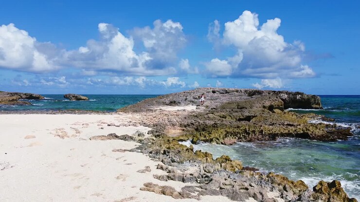Ripresa aerea di una giovane ragazza in abito bianco che cammina su una roccia gigante lungo la costa tropicale a Cozumel, Messico, in una soleggiata giornata estiva.