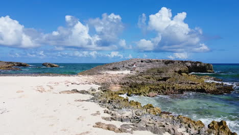 aerial-of-young-girl-in-white-dress-walking-on-giant-rock-along-tropical-shoreline-in-Cozumel-Mexico-on-sunny-summer-day