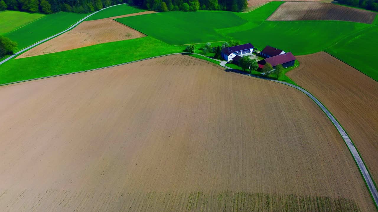 vista aérea de un gran campo arado con tierras de cultivo verdes circundantes y edificios rurales