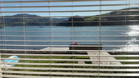 a tranquil lakeside scene viewed through window blinds, capturing sunlight reflecting on water in akaroa, new zealand