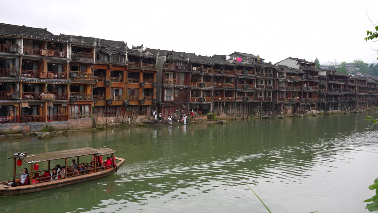 Tourists on a boat glide along Tuojiang River by historic Stilted Buildings in Fenghuang, China