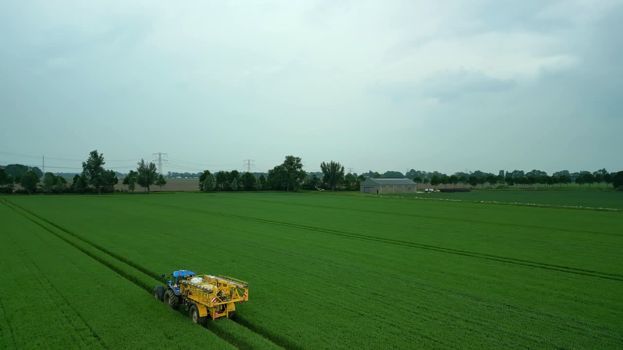 접힌  스프레이어 를 가진 트랙터 는 아직도 초록색 의 곡물  을 가로질러 운전 한다