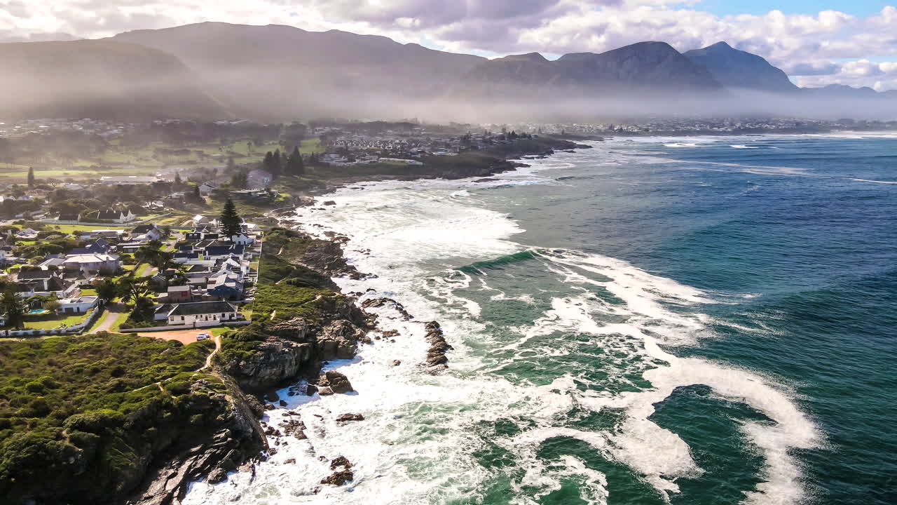 Drone hyperlapse of sea foam floating near Hermanus coastline as waves roll in