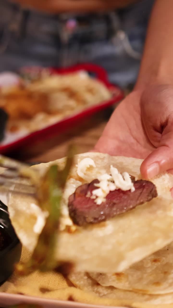 Mani assemblano tlayudas con carne alla griglia, formaggio e verdure in un vivace ambiente di ristorante.