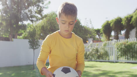 portrait of happy caucasian boy holding football in garden, slow motion