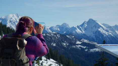 woman views the snowy mountains through binoculars during winter. medium shot