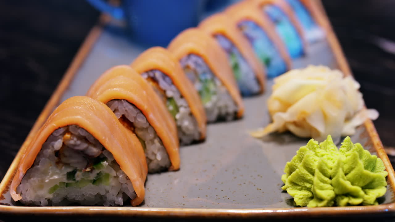 Close up of triangle shaped salmon sushi on a platter with wasabi and gari