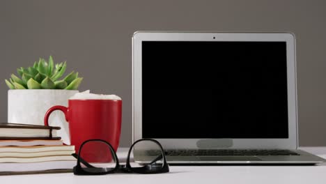 Laptop,-spectacles,-cup-of-coffee-and-stack-of-books