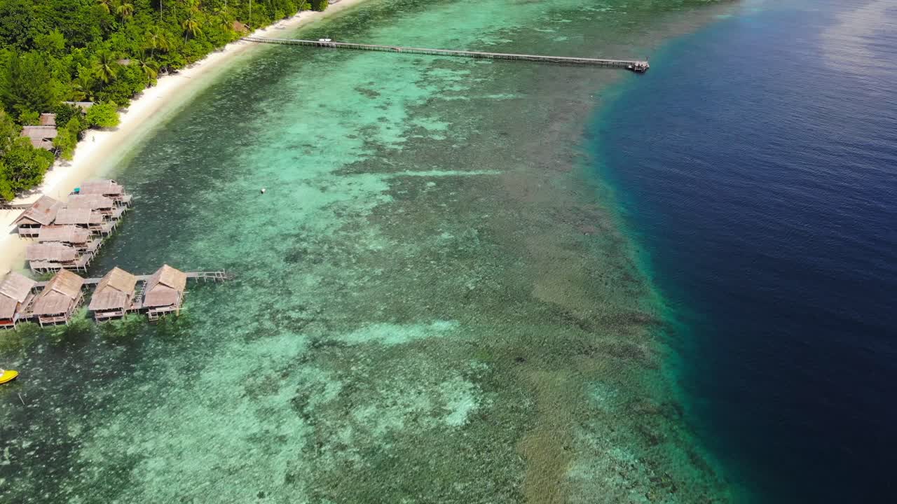 aguas claras de color turquesa y azul frente a una playa de arena con pasarela de madera, muelle y casas de huéspedes de madera, casa de huéstedes lumba lumba en la isla de kri en raja ampat, indonesia