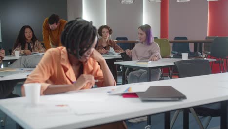 en el fondo los estudiantes están sentados en los escritorios y hablando juntos mientras su maestro está comprobando su tarea