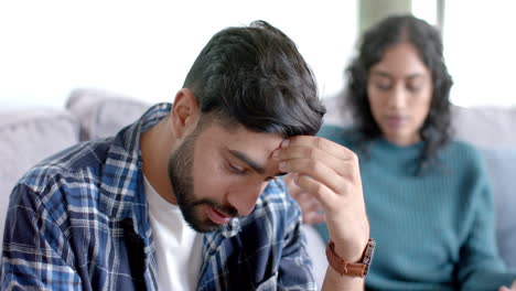 una pareja biracial sentada en el sofá y discutiendo en casa, en cámara lenta.