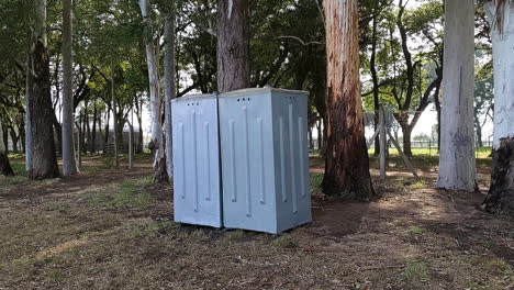 viajando fuera del baño portátil gris rodeado de árboles en un día soleado
