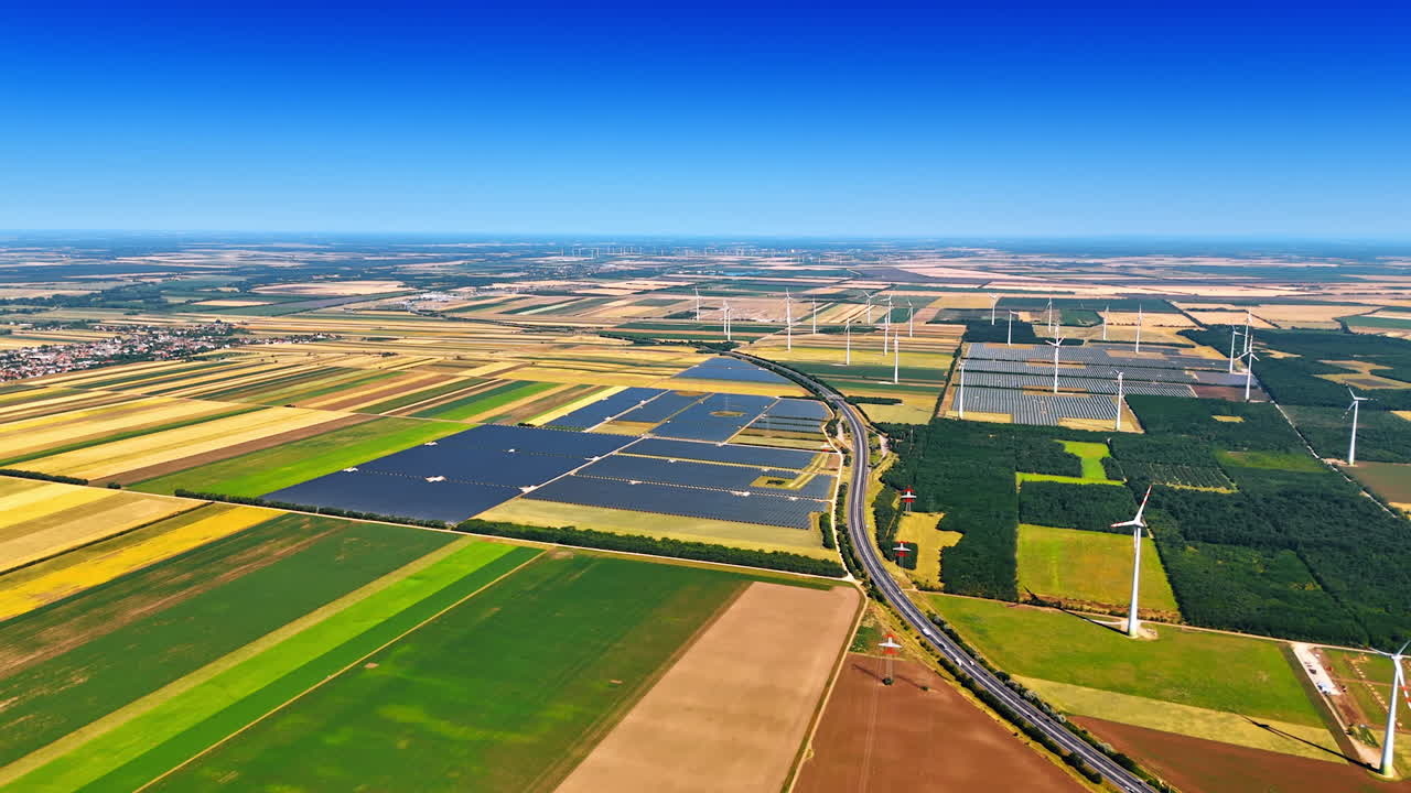 Vast plain nature landscape divided into colorful patches. Wind farms and solar panels installed in the scenery. Aerial view