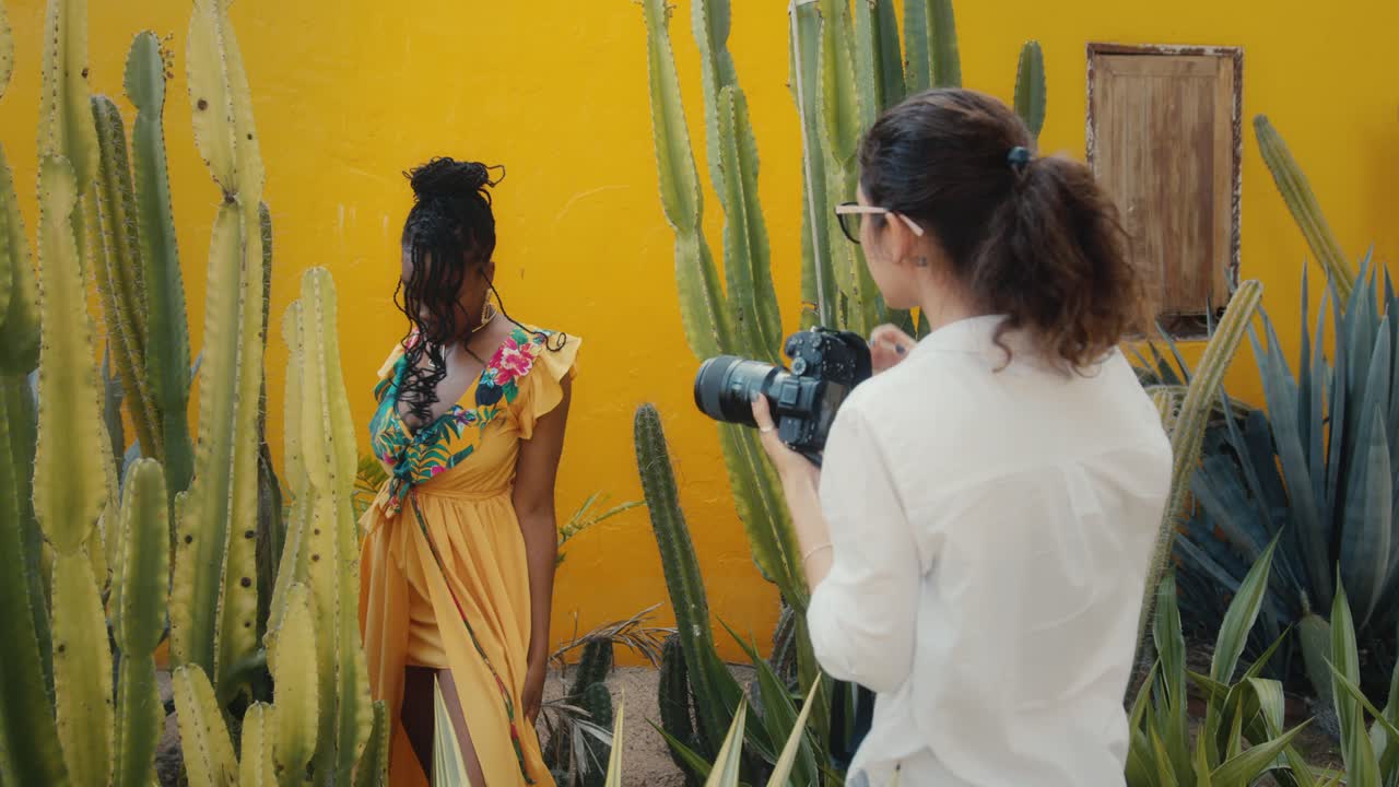 Fashion photoshoot with a model in front of a yellow wall, surrounded by cacti