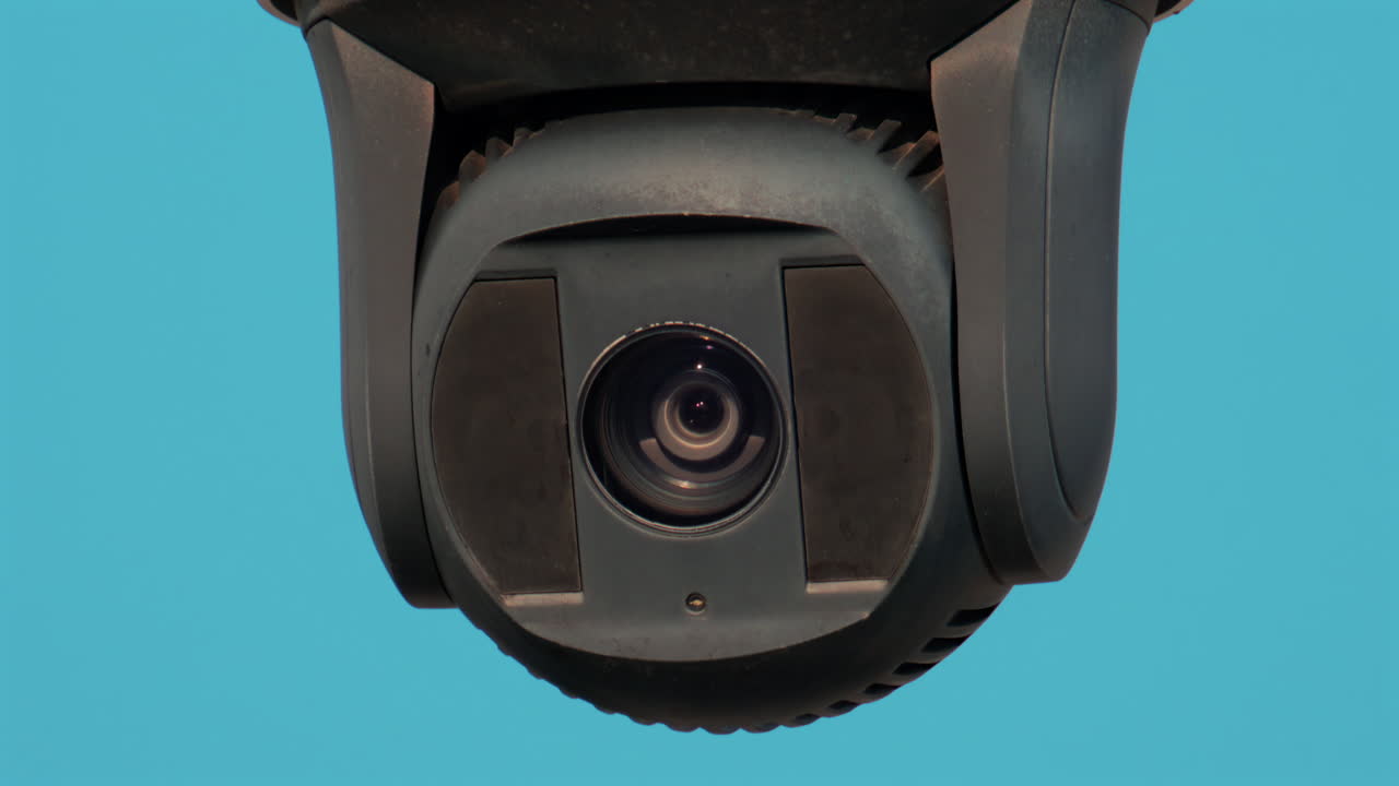 A close up of a modern black surveillance camera turning against a bright sky background