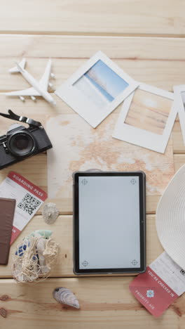 Vertical video of tablet with copy space, camera, passport and sunhat on wooden background