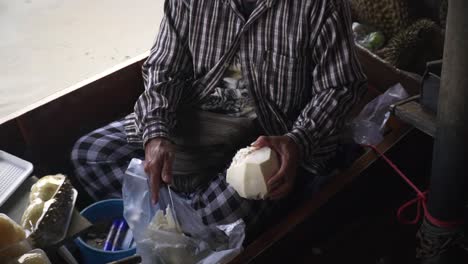 local vendor peeling off fruit using knife on his boat at damnoen saduak floating market in ratchaburi, thailand, static closeup