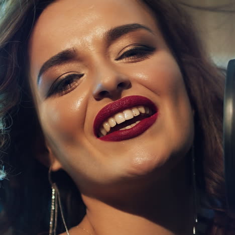 attractive face of a professional singer near microphone looking at camera and singing at music studio. portrait of a beautiful female and mic. close-up