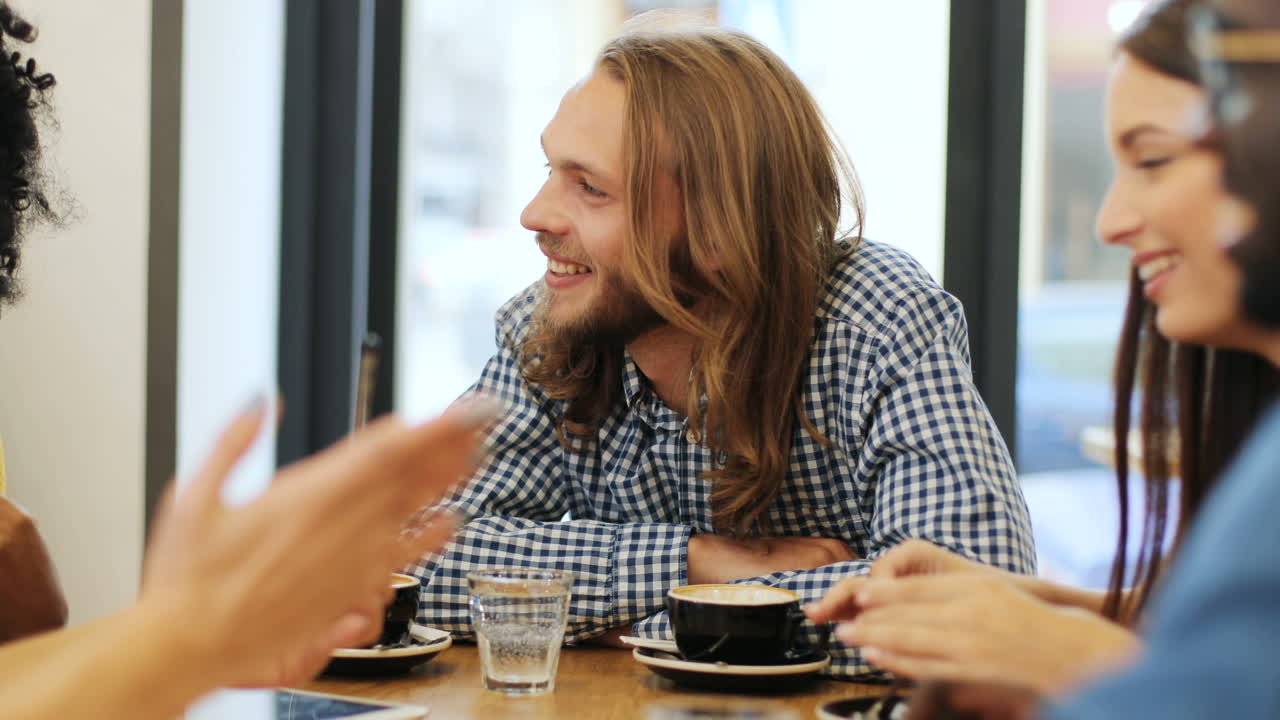 vista cercana de un grupo multiétnico de amigos hablando y riendo sentados en una mesa en un café