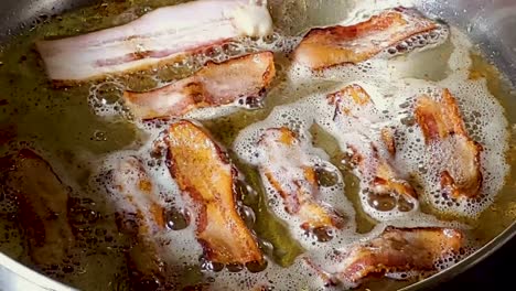 close-up of a slice of bacon added to fried bacon on pan