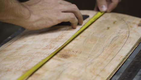 hand of craftsman working on wooden skateboard with yellow measure tape