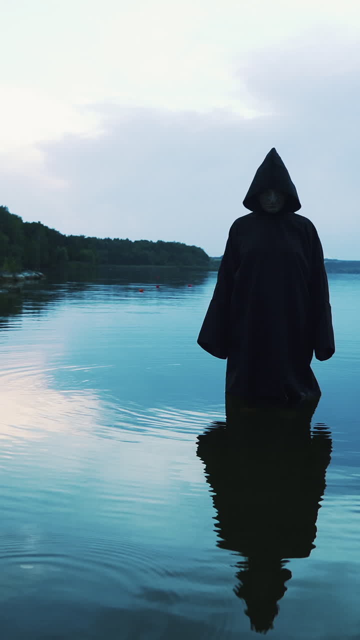 Scary figure in black mantle in the river. Halloween costume.. Vertical video