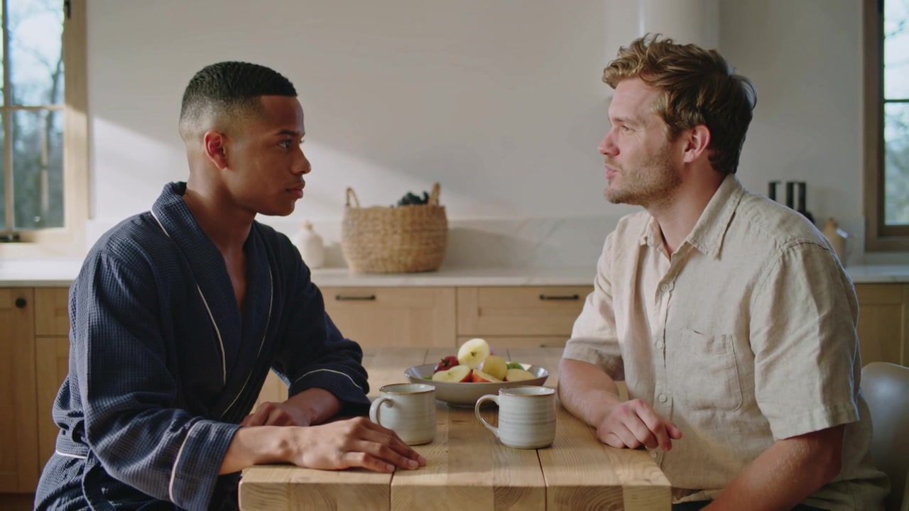 Speaking right man leaning after eye contact at kitchen table, sharing concern, beige shirt, mugs