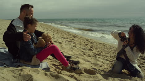 joyful family taking photos on ocean beach sand. people relax together on sand.