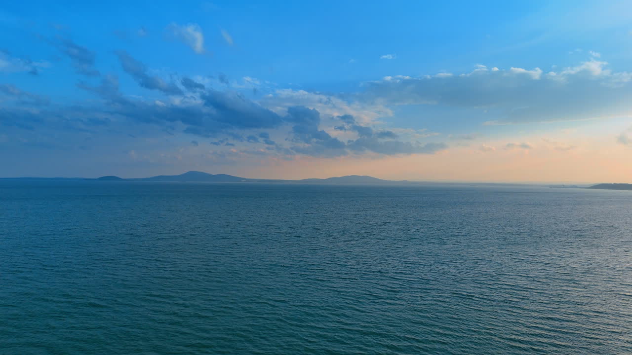Cielo sereno sopra l'oceano aperto al tramonto. La luce del sole si estende sull'oceano mentre il sole tramonta all'orizzonte. Le onde increspano dolcemente sotto un cielo vasto.