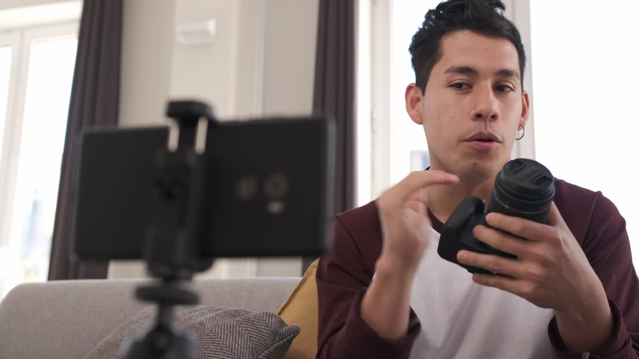 Giovane uomo latino che parla alla fotocamera del cellulare, spiegando una macchina fotografica. Concetto di content creator