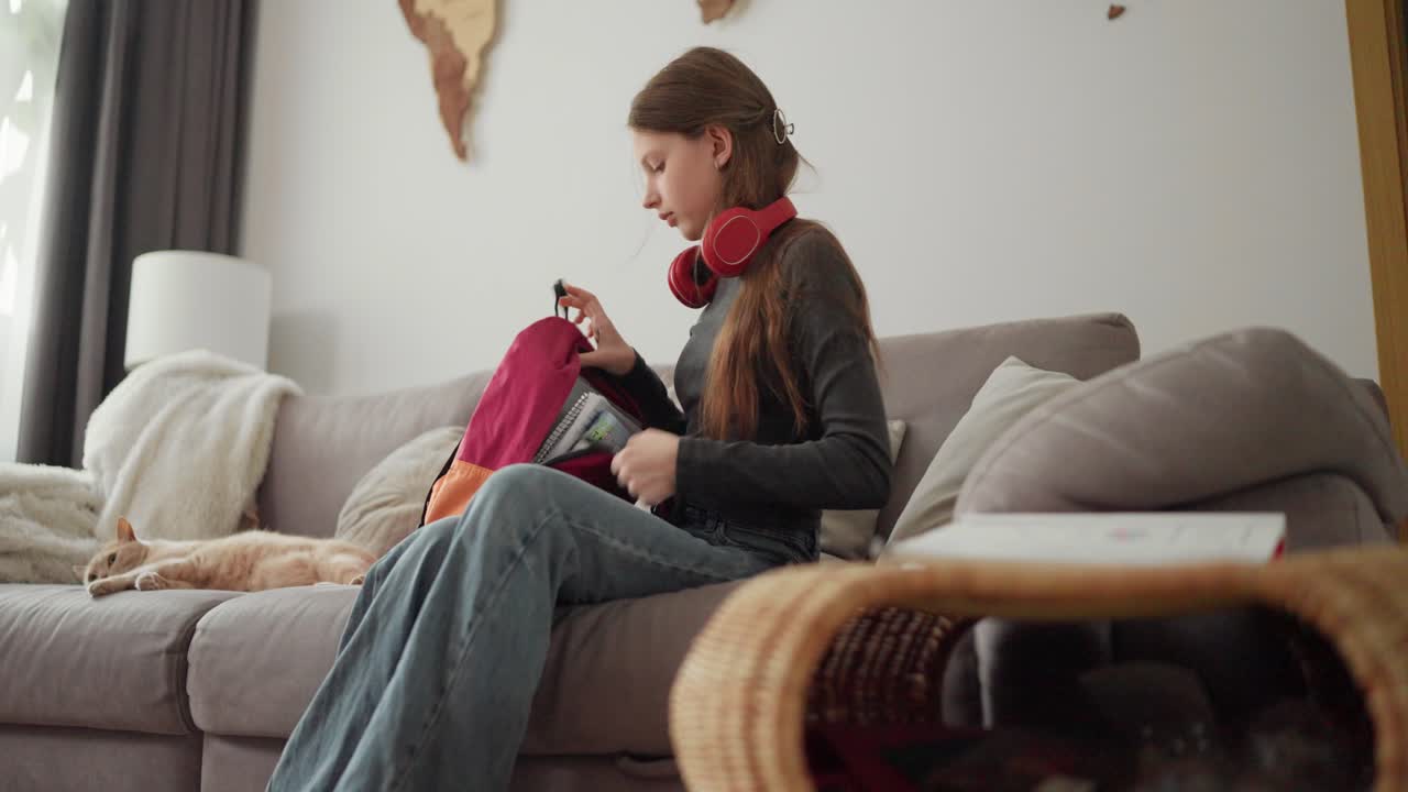 Woman with headphones reading on couch with cat and backpack