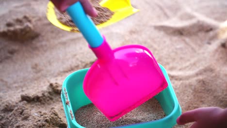 le mani di un bambino che gioca con la sabbia della spiaggia con una pala e un secchio