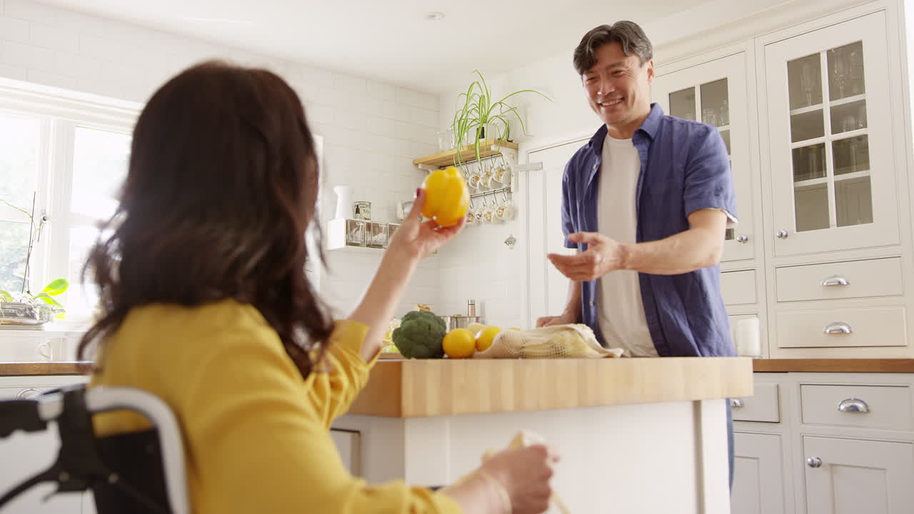 ⁇ 체어에 앉은 아내와 함께 성숙한 아시아 커플이 쇼핑 여행 후 부 ⁇ 에서 신선한 제품을 풀고 있습니다. 느린 속도로 촬영되었습니다.
