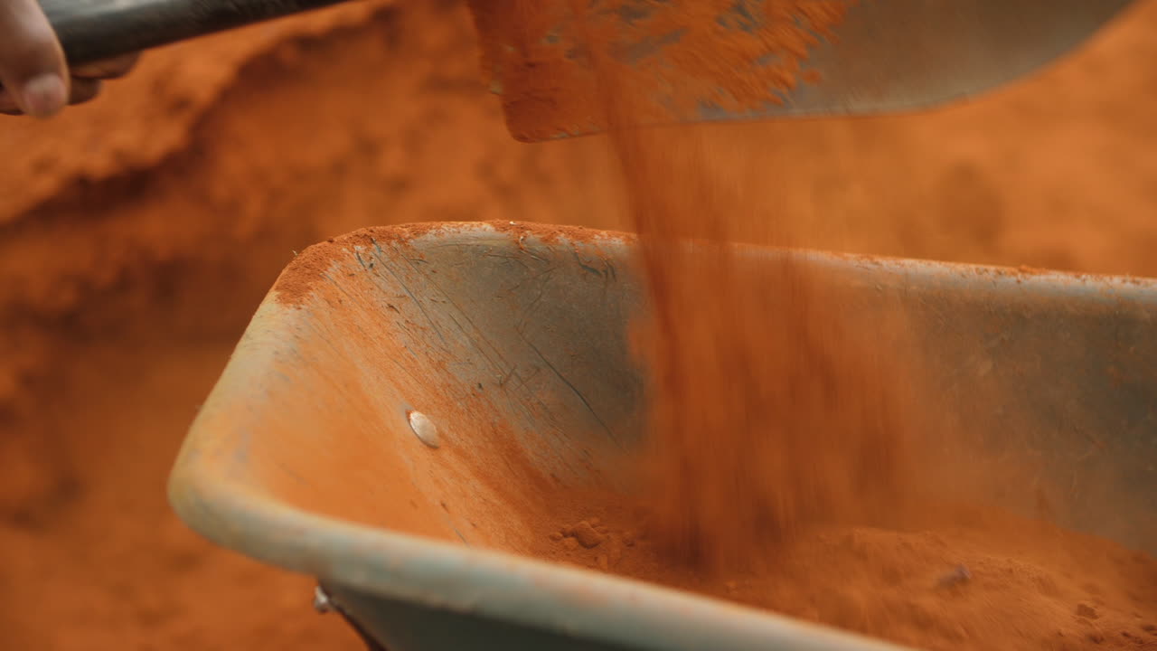 Construction Worker Moving Red Dirt with Shovel and Wheelbarrow