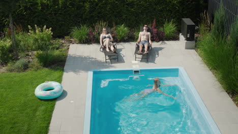 a family with a child relaxes by the small pool in their villa. parents sunbathe, child swims