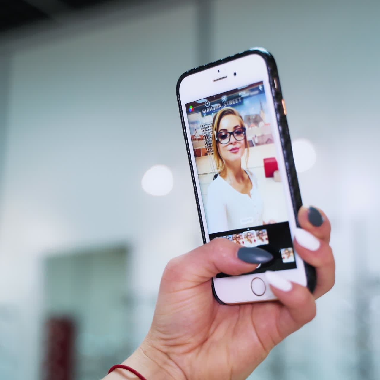 Woman looks at herself in the mobile phone. Female's hand holding phone and showing the video with a beautiful woman in eyeglasses.