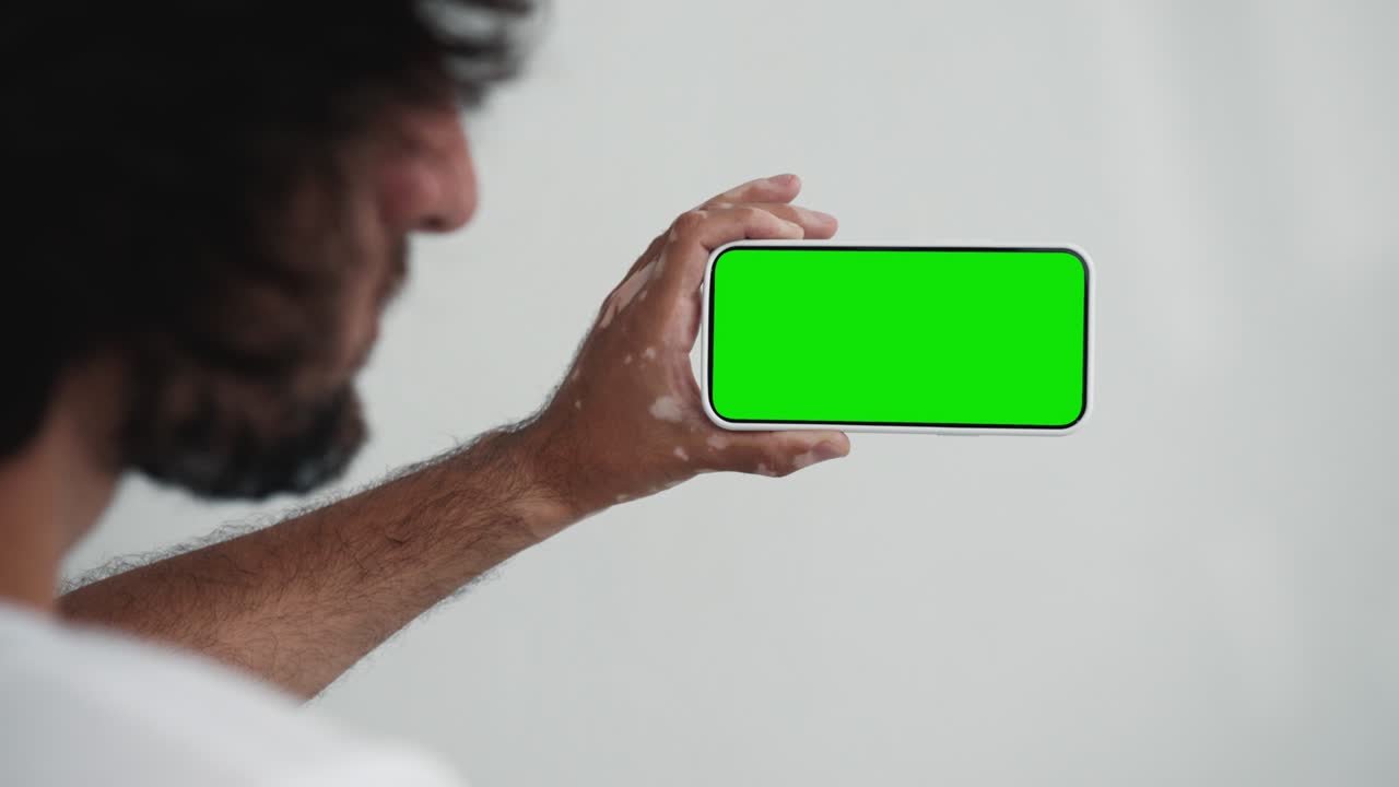 joven utiliza un teléfono inteligente con pantalla verde chroma clave de primer plano. hombre sostiene en la mano un modelo de teléfono celular. concepto ver y mostrar internet redes sociales, llamadas de video, leer noticias, aplicación, compras electrónicas, película 4k
