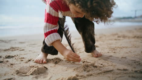 Niño-Pequeño-Dibujando-Arena-Con-Primer-Plano-De-Plumas-De-Pájaro.-Niño-Concentrado-Descansando-En-La-Playa