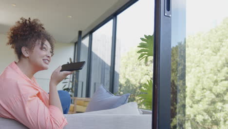 smiling woman holding smartphone, sitting on couch, enjoying leisure time, copy space