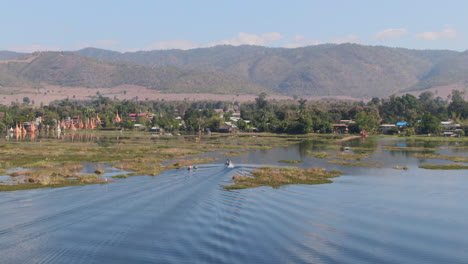 Aerial-view-showing-traditional-long-tail-boat-arriving-Taw-Mwe-Khaung-Pagoda-on-Moebyel-Lake,-Myanmar