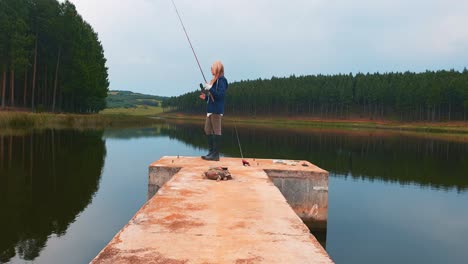 a woman fishing for bass from a pier in a beautiful forest lake