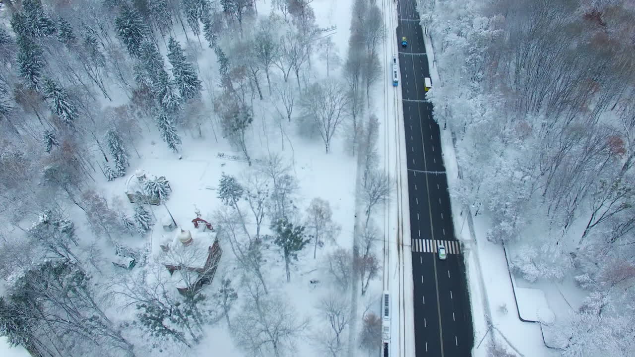 Black two-lane road standing out at the white backdrop of the city landscape. Winter in the city from aerial perspective.